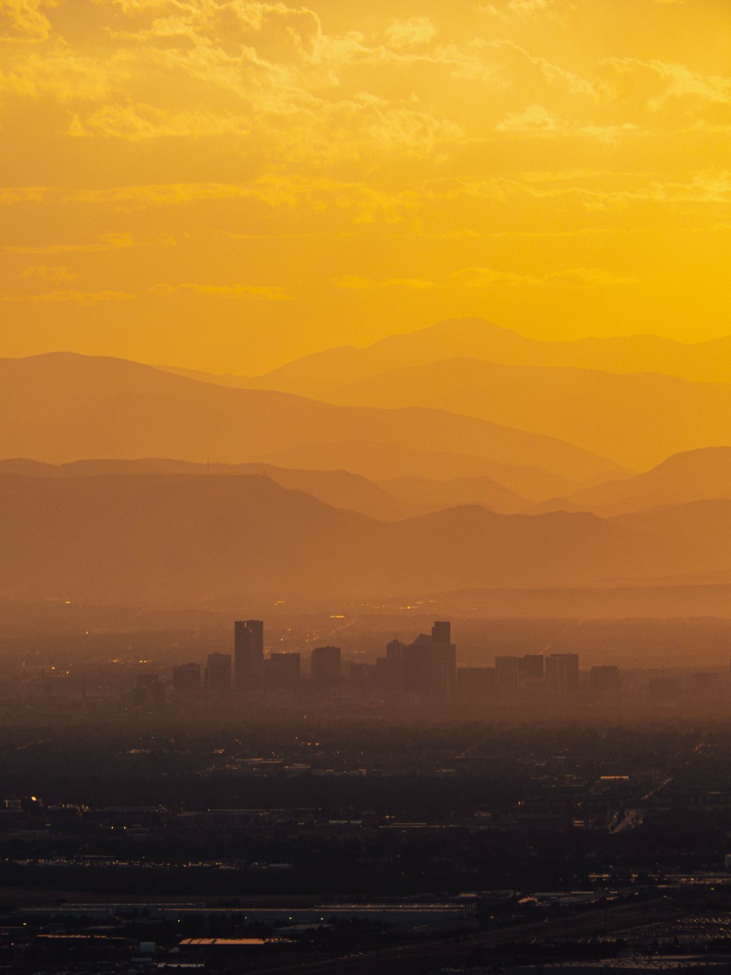 Layers of foothills glowing behind the Denver skyline at golden hour
